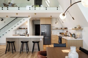 Eine moderne Küche mit Kochinsel, Barhocker, Esstisch und einer Treppe zu einer oberen Ebene.