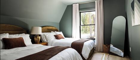 A bedroom with two beds, a nightstand, a lamp, a window with curtains, and a mirror.