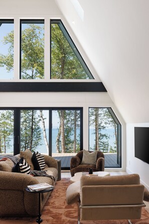 Ein modernes Wohnzimmer mit großen Fenstern, einem Sofa, einem Sessel und einem Couchtisch.