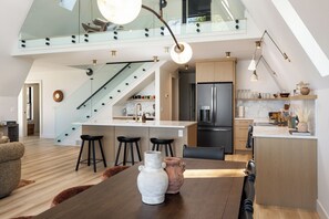 Eine moderne Küche mit einer zentralen Kochinsel, einer Essecke mit Holztisch und einer Treppe, die in einen oberen Bereich führt.