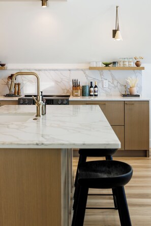 Eine moderne Küche mit Marmorarbeitsplatte, Edelstahlgeräten und einer Holztruhe mit einem schwarzen Hocker.