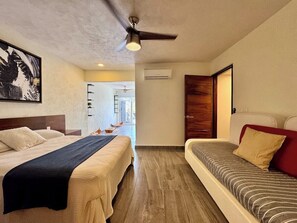 Ein Hotelzimmer mit einem Bett, einer Couch, einem Deckenventilator, einer Klimaanlage und einem Bild an der Wand.