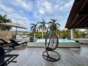 Zona de piscina al terrat amb gandules, una cadira penjant i vistes a palmeres i un port esportiu.