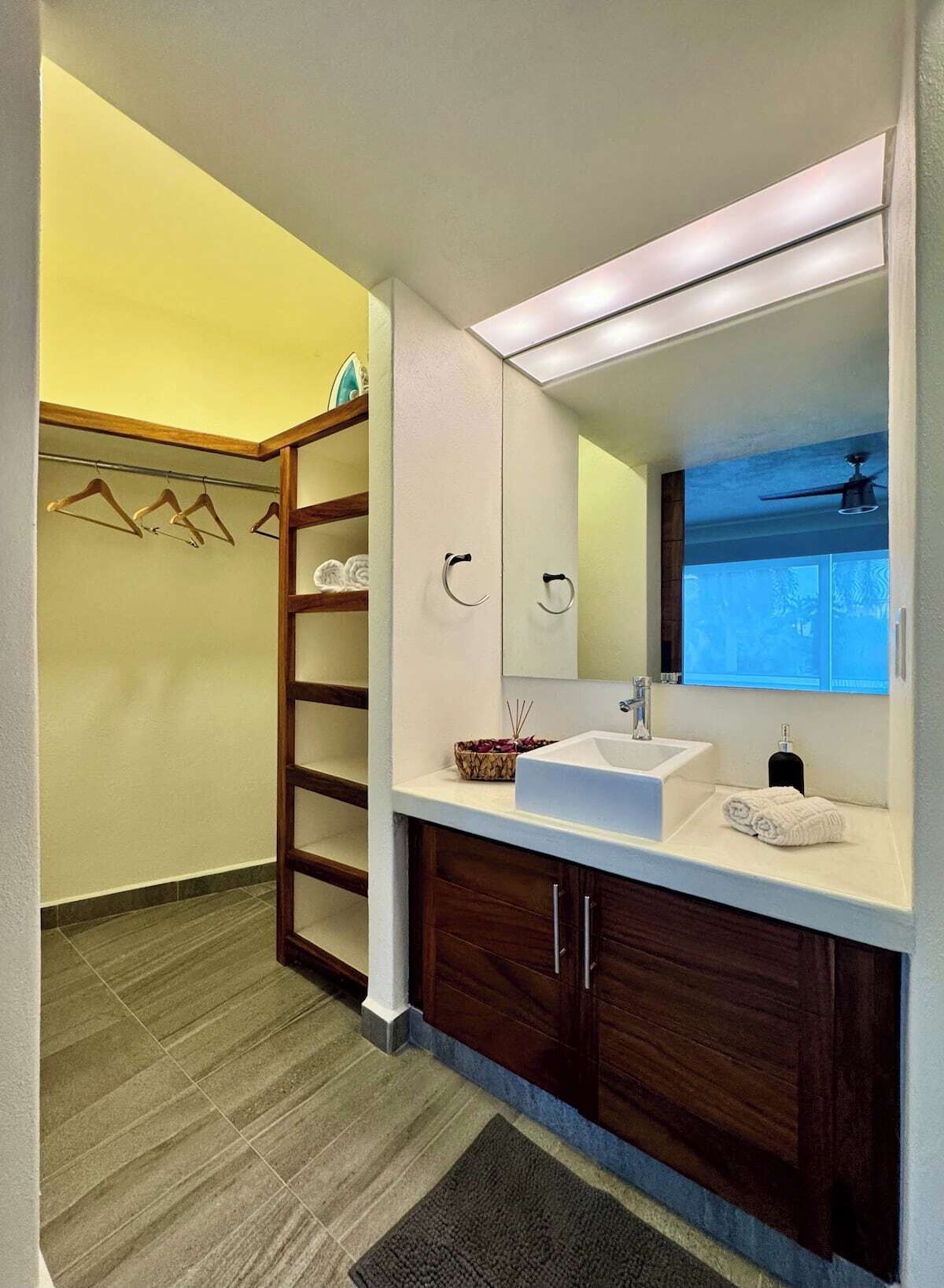 Une salle de bain avec un lavabo blanc, des meubles en bois foncé, un miroir et un porte-serviettes.