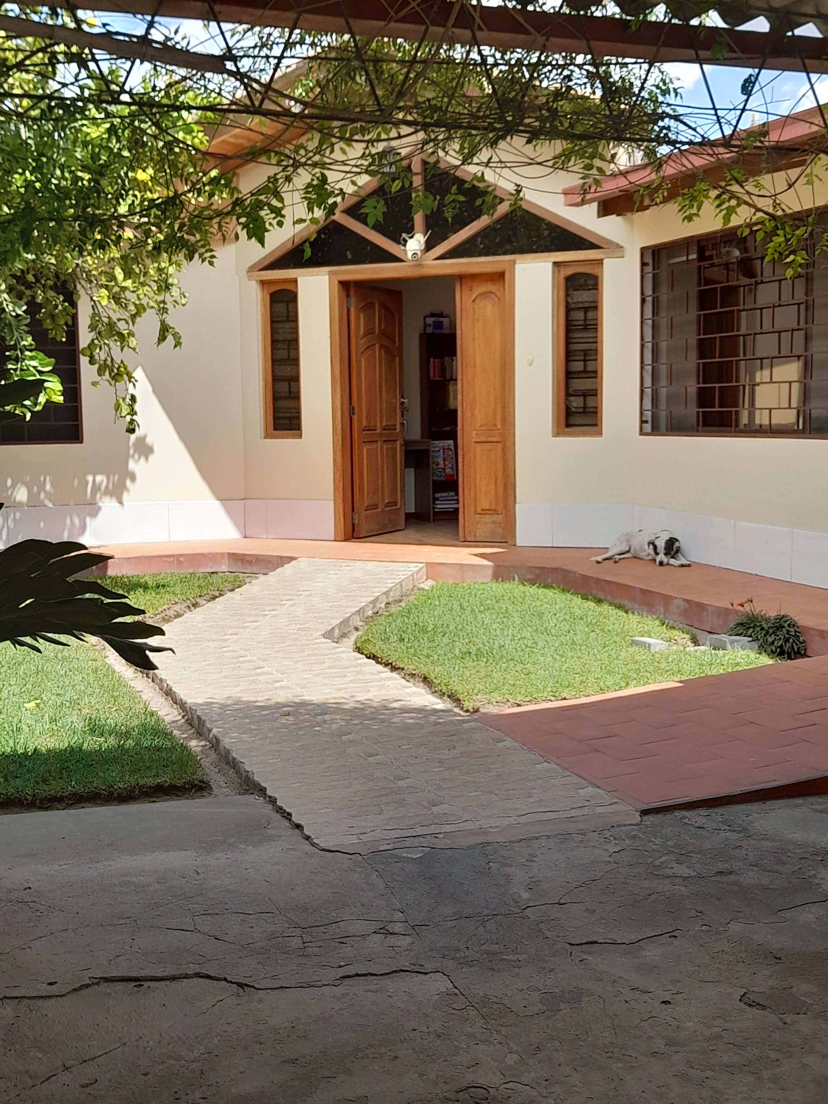 A building with a wooden door, a small garden area with grass, and a paved walkway leading to the entrance.