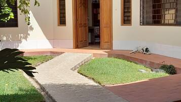 A building with a wooden door, a small garden area with grass, and a paved walkway leading to the entrance.