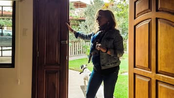 Une porte en bois avec un loquet métallique, une personne debout dans l’embrasure de la porte et un chien tenu en laisse à l’extérieur.
