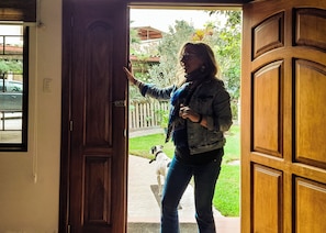 A wooden door with a metal latch, a person standing in the doorway, and a dog on a leash outside. - Rose Garden. "Tu refugio, tu experiencia inolvidable" Ubicado en Guayllabamba. (Guayllabamba)