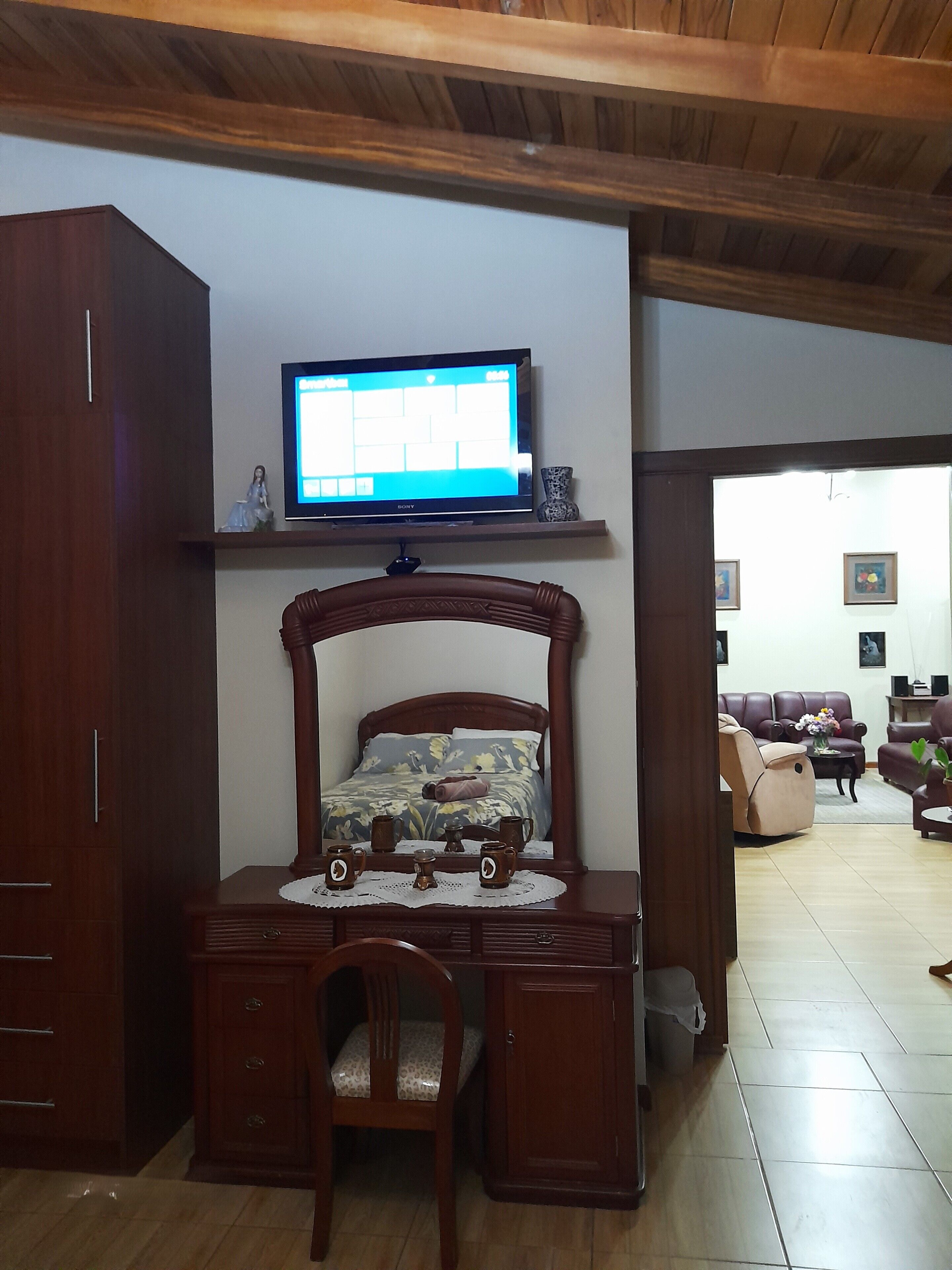 Un dormitorio con una cama de madera, un televisor en una estantería, un escritorio con una silla y un armario.