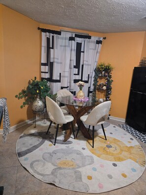 A dining area with a round table, four chairs, a vase with flowers, a potted plant, and a decorative wall piece. - Private Basement Suite with Kitchen & Separate Entrance (Upper Marlboro)