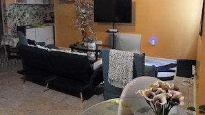 A living room with a sofa, a glass coffee table, a TV, and a ceiling fan.