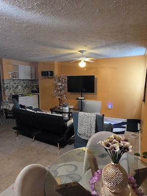 A living room with a sofa, a glass coffee table, a TV, and a ceiling fan.