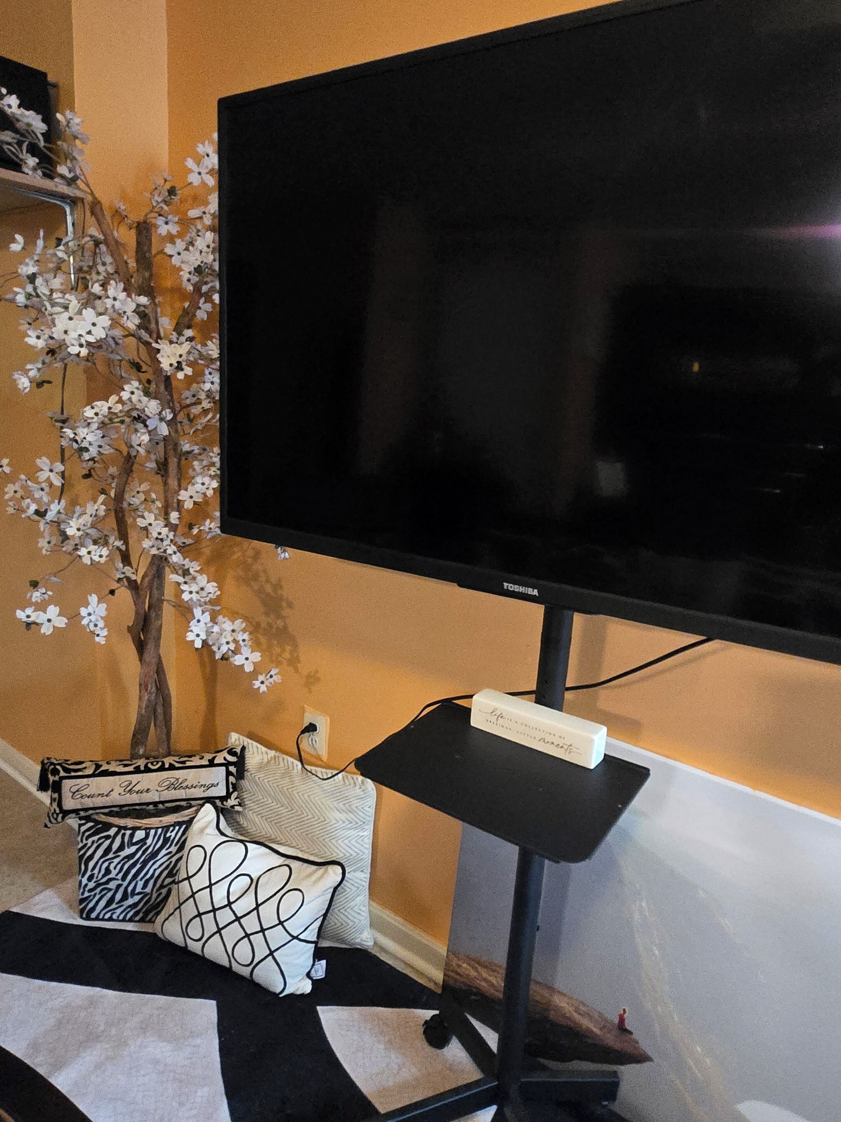 A television on a stand with a decorative tree and pillows.