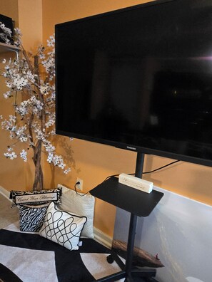 A television on a stand with a decorative tree and pillows.