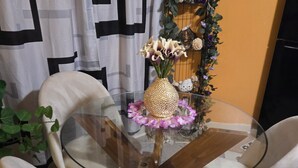 A dining area with a glass table surrounded by four chairs, a vase with flowers, and a decorative wall piece.