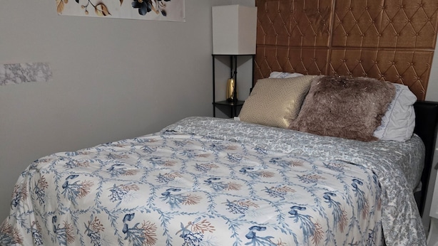 A bedroom with a bed, a headboard, a nightstand, a lamp, and a wall art piece.