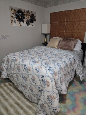 A bedroom with a bed, a headboard, a nightstand, a lamp, and a wall art piece. - Private Basement Suite with Kitchen & Separate Entrance (Upper Marlboro)