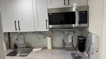 A kitchen with white cabinets, a stainless steel sink, a microwave, and a coffee maker.