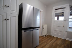 A kitchen with white cabinets, a stainless steel refrigerator, and a white radiator. - Chicago Life Apartment - 3 bedroom (Chicago)