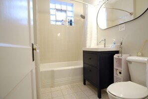 Un baño con una bañera blanca, un tocador negro con un espejo y un inodoro blanco.