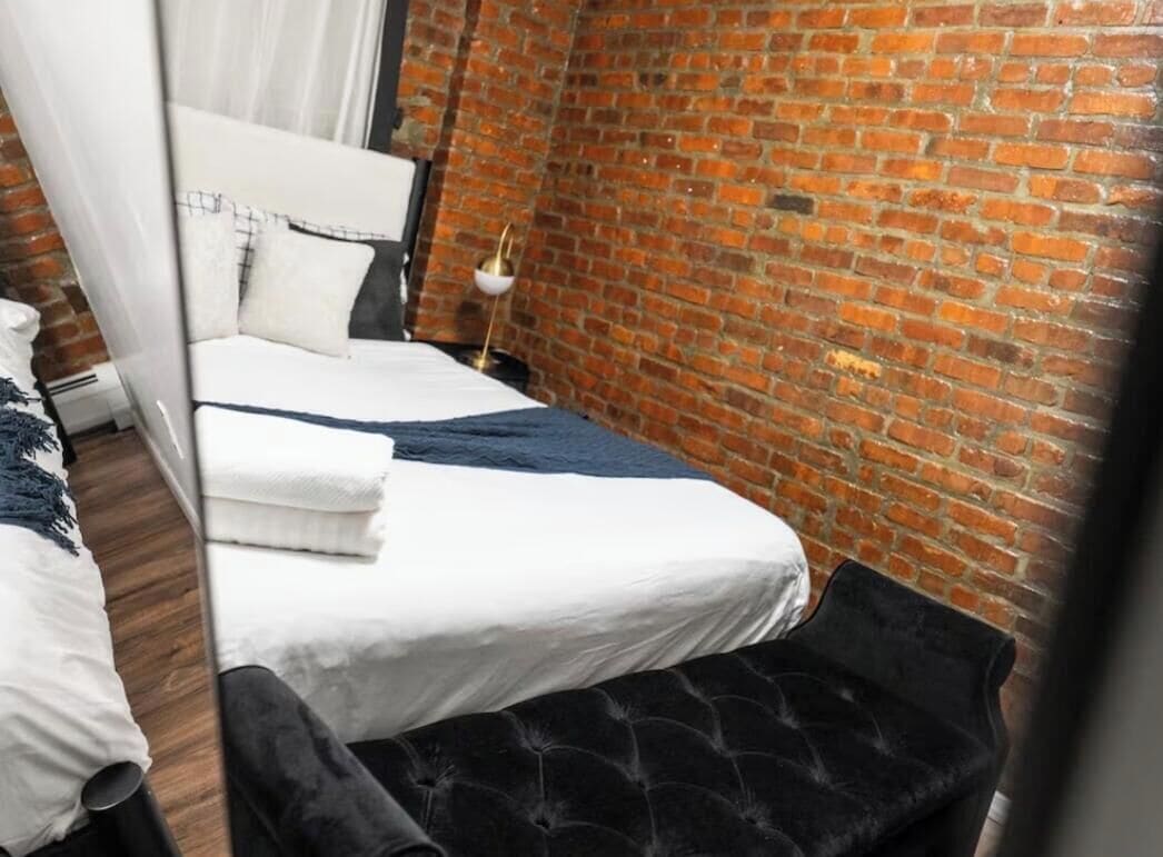 Una habitación con una cama, una mesita de noche, una lámpara y una pared de ladrillo.