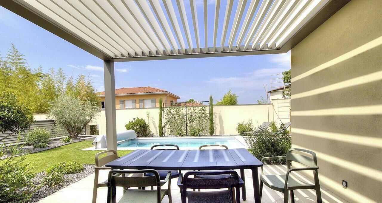 En udendørs terrasse med swimmingpool, et bord og stole.