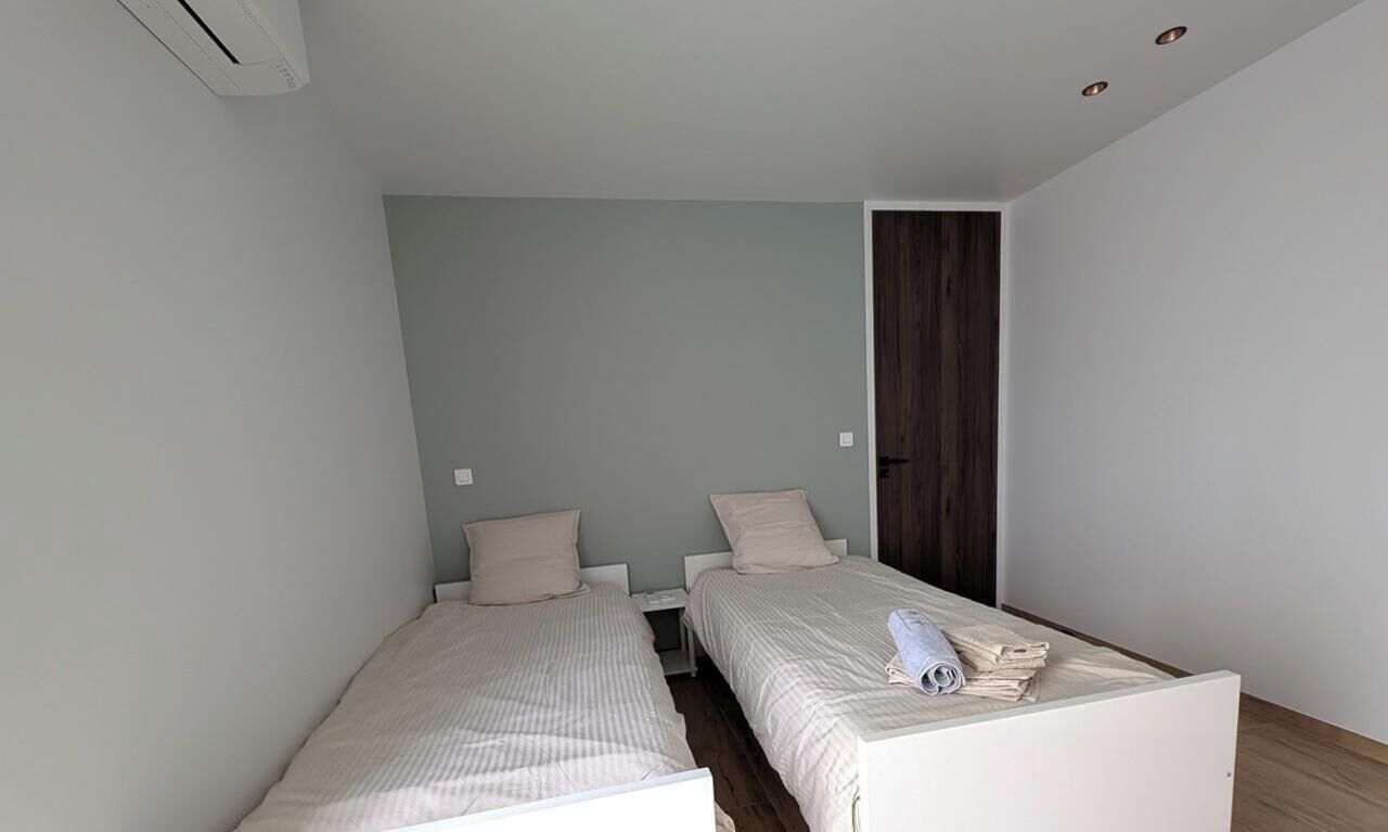 Ein kleines, modernes Zimmer mit zwei Einzelbetten, einer Holztür und einer weißen Klimaanlage.