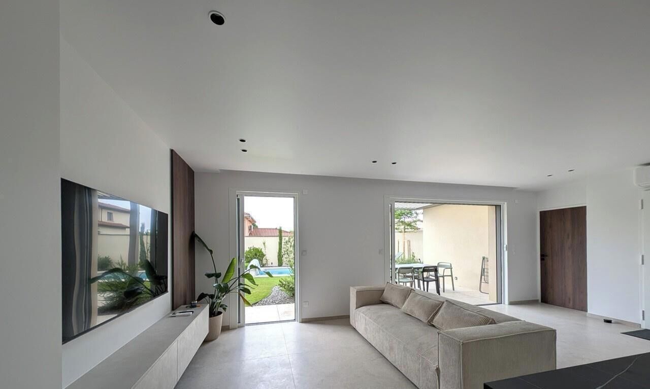 Un soggiorno moderno con un divano, una televisione e una grande finestra vista giardino.