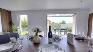 Un coin repas avec une table dressée pour quatre personnes, une bouteille de vin et un vase rempli de fleurs.