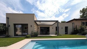 Une maison moderne dotée d’une piscine, d’un patio et d’un espace extérieur aménagé et couvert.