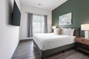 A hotel room with a bed, a bedside table with a lamp, a TV mounted on the wall, and a window with curtains.