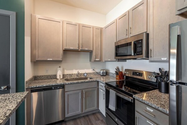 A modern kitchen with stainless steel appliances, granite countertops, and wooden cabinets.