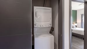 A compact laundry area with a washing machine and dryer, a door leading to a bedroom with a bed and a nightstand. - Landing Amazing 2bd, Courtyard, Clubhouse (Dayton)