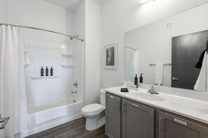 Un bany modern amb un box de dutxa de vidre, un vàter blanc, un lavabo amb un mirall i un armariet amb etiquetes per draps i tovallons.