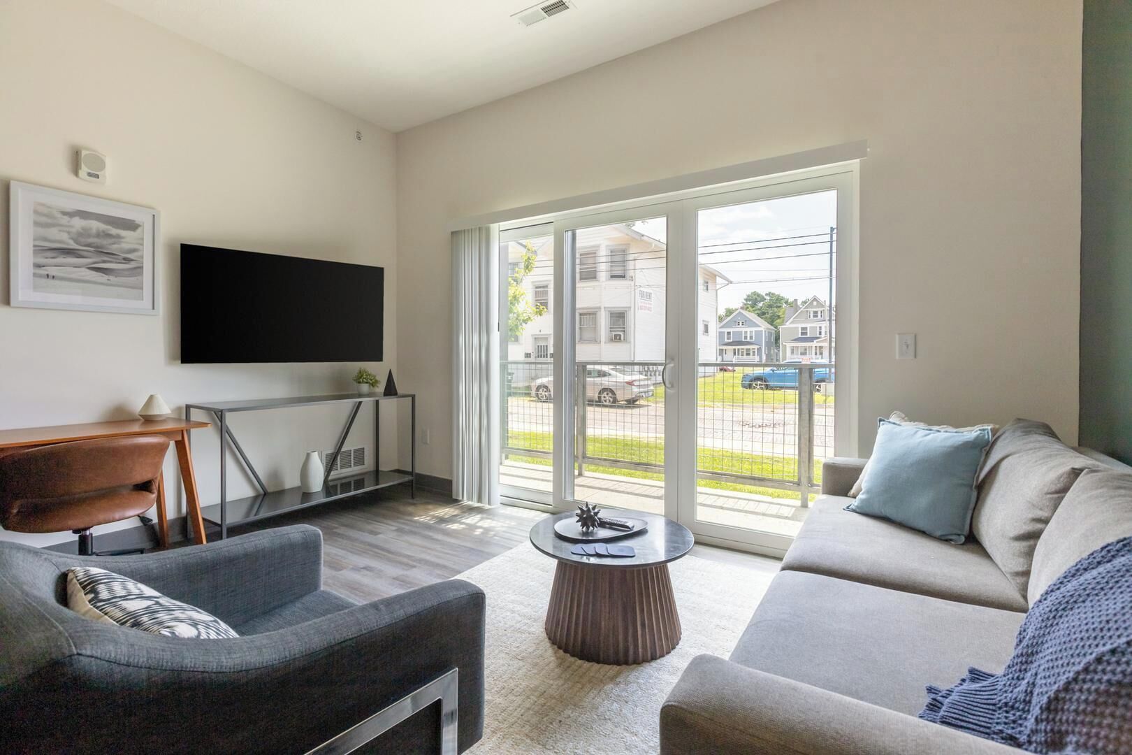 A modern living room with a sofa, armchair, coffee table, and a flat-screen TV mounted on the wall.
