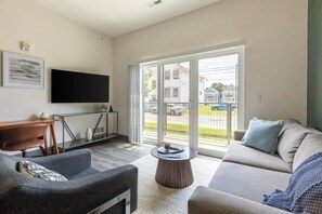 A modern living room with a sofa, armchair, coffee table, and a flat-screen TV mounted on the wall.