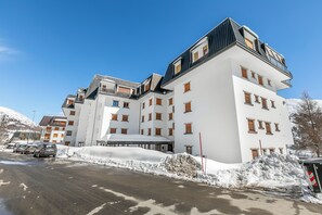 Een hotel met meerdere verdiepingen, met een modern architectonisch ontwerp, voorzien van balkons en een skipiste op de achtergrond.