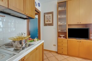 A compact kitchen with wooden cabinets, a built-in stove, and a flat-screen TV.