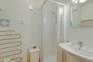 Un bany amb dutxa trencada per vidre, un lavabo blanc i una barra de tovalloles.