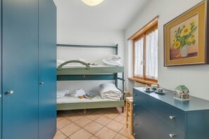 Un llit superposat amb tovalloles ben arrufades, una taula petita amb una tetera i un quadre amb girassols a la paret.