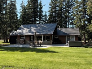A modern house with a sloped metal roof, a patio with outdoor furniture, and a large window.