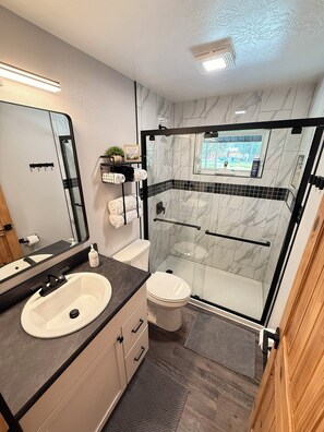 A modern bathroom with a white sink, toilet, and glass-enclosed shower.