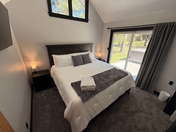 A neatly made bed with a headboard, a bedside lamp, and a view of the outdoors through a window.