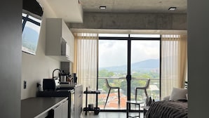Quarto de hotel moderno com cozinha compacta, cama, varanda com vista e área de refeições.