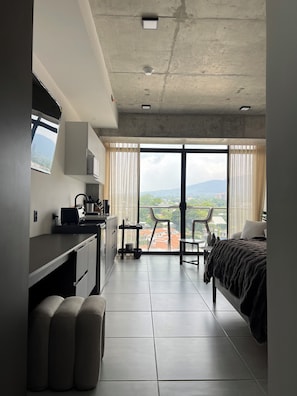 Una habitación de hotel moderna con kitchenette, una cama, un balcón con vistas y una zona de comedor.