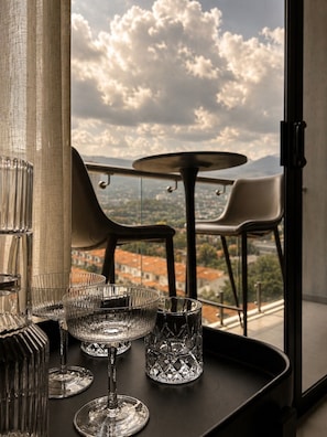 Un balcón con mesa y sillas, con vistas a un paisaje urbano y montañas.