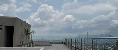 Eine Dachterrasse mit freiem Blick auf die Stadtlandschaft, einer Glasumlaufung und einigen Palmen.