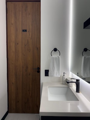 Un baño con puerta de madera, un lavabo blanco, un espejo y un perchero para toallas.