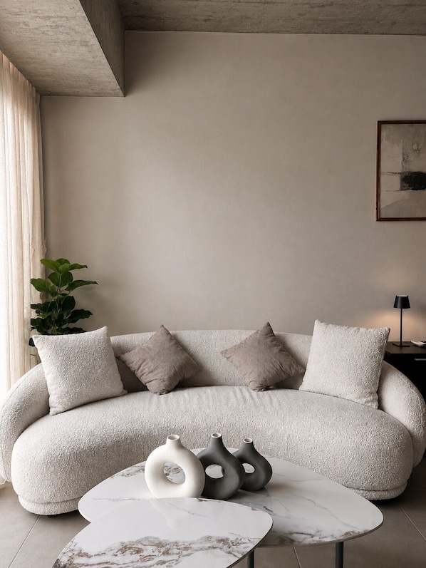 Una sala moderna con sofá, cojines, una mesa de centro y jarrones decorativos.
