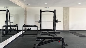 Uma academia com equipamentos de musculação, um banco e um espelho na parede.